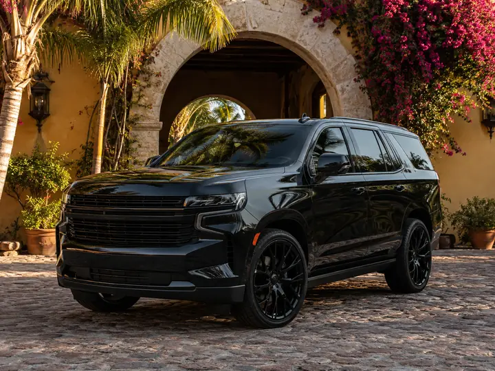 A blacked out full size SUV on a cobblestone drive in front of a stone villa arch.